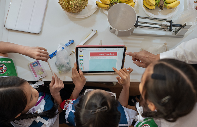 Three primary students gather around iPad to collaborate on a presentation for a science project.