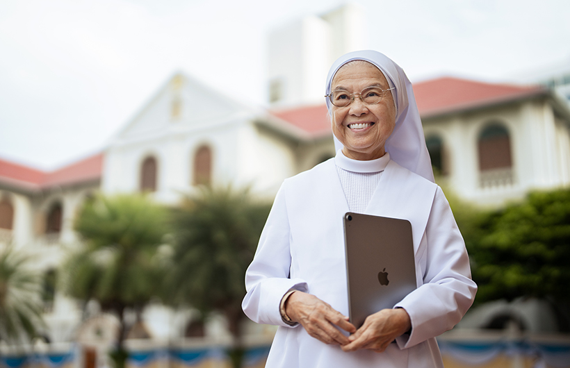 Principal Sister Françoise Jiranonda stands outside the school holding her iPad.